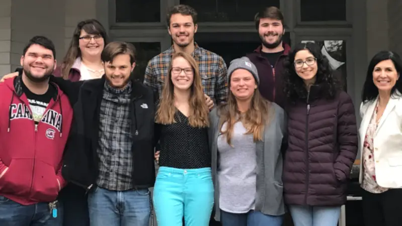 A person hands a small box to another individual while exchanging items at a vibrant market filled with clothing and decorative objects